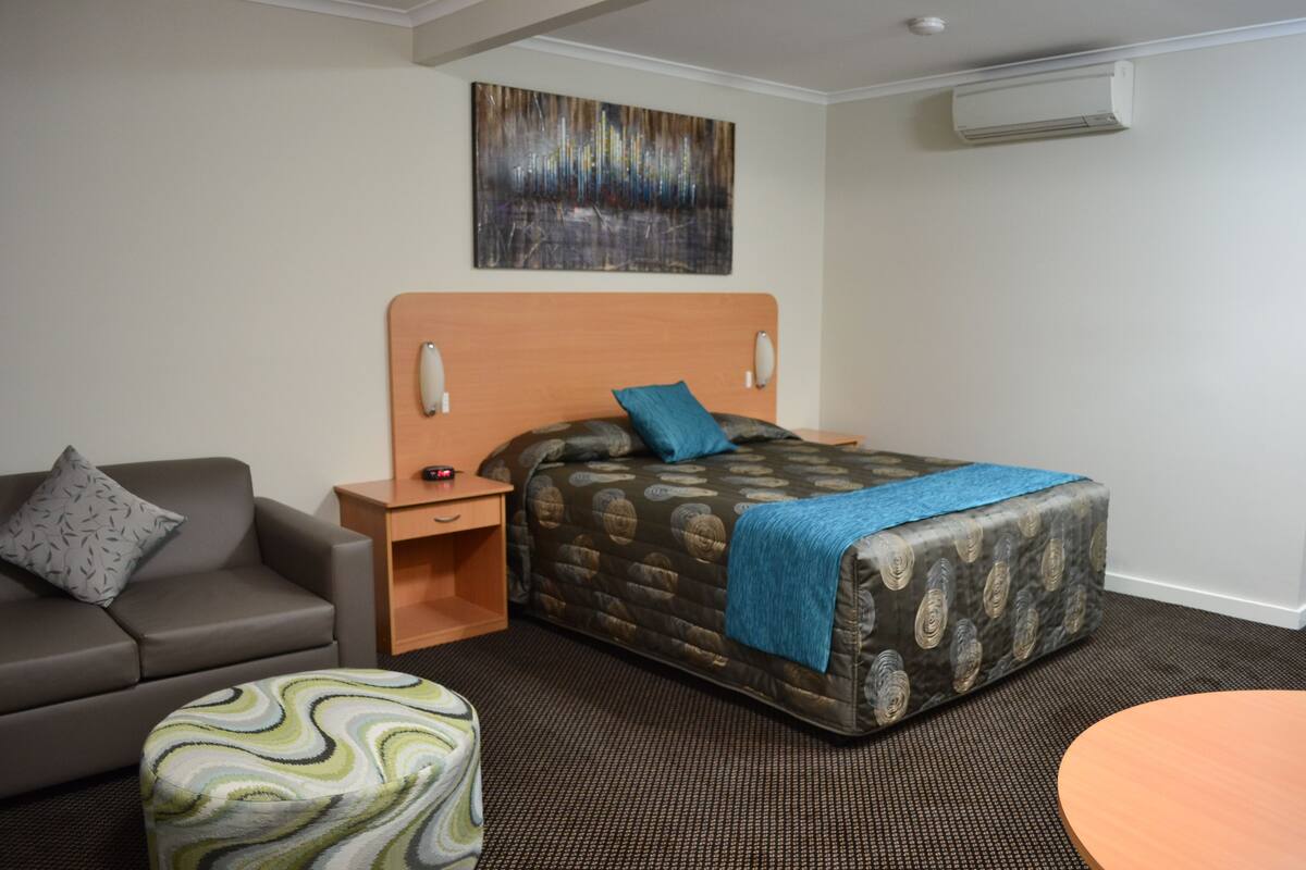 Une chambre d’hôtel équipée d’un lit, d’un canapé, d’une petite table et d’un climatiseur fixé au mur.