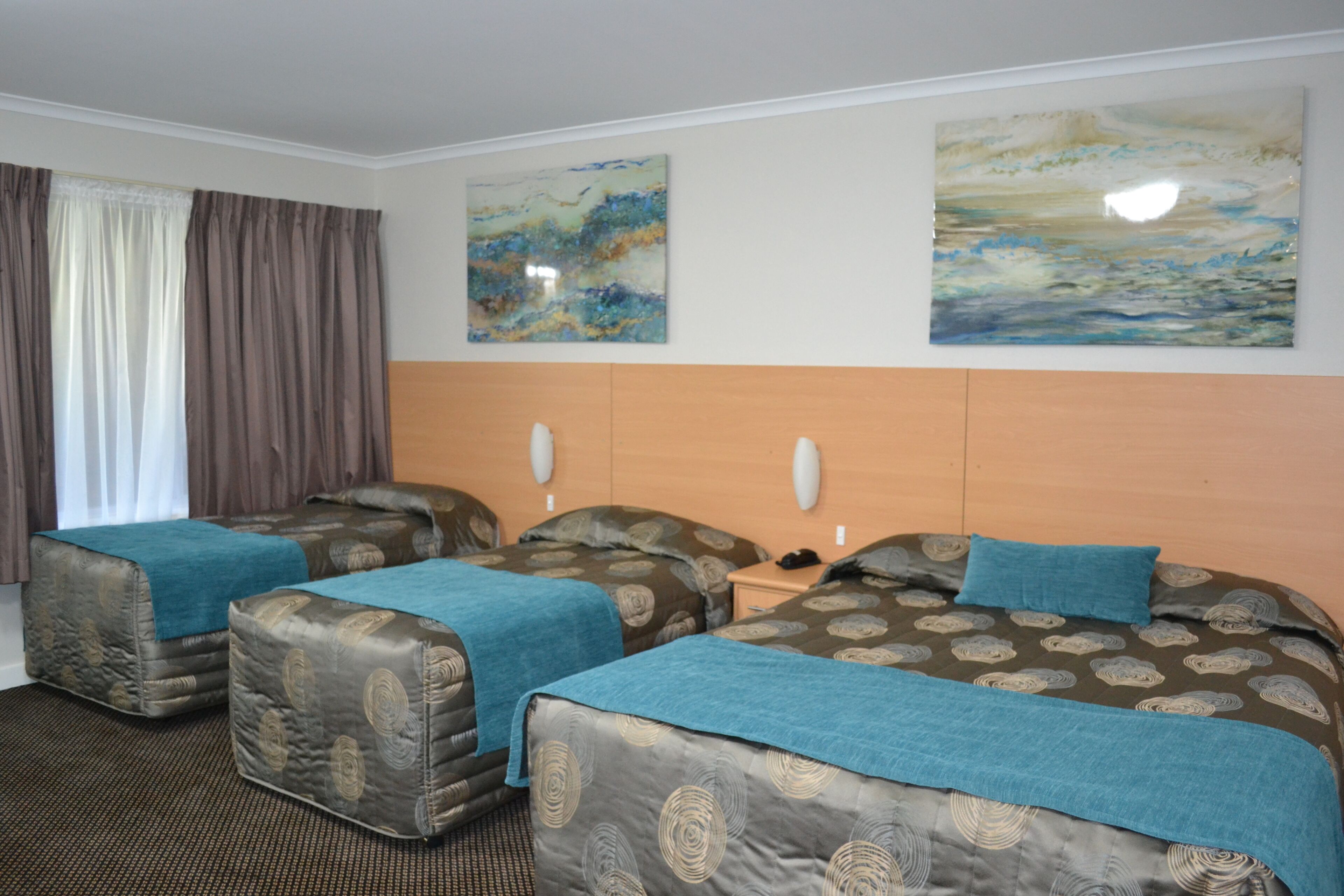 Een hotelkamer met twee eenpersoonsbedden, een houten hoofdbord en twee abstracte schilderijen aan de muur.