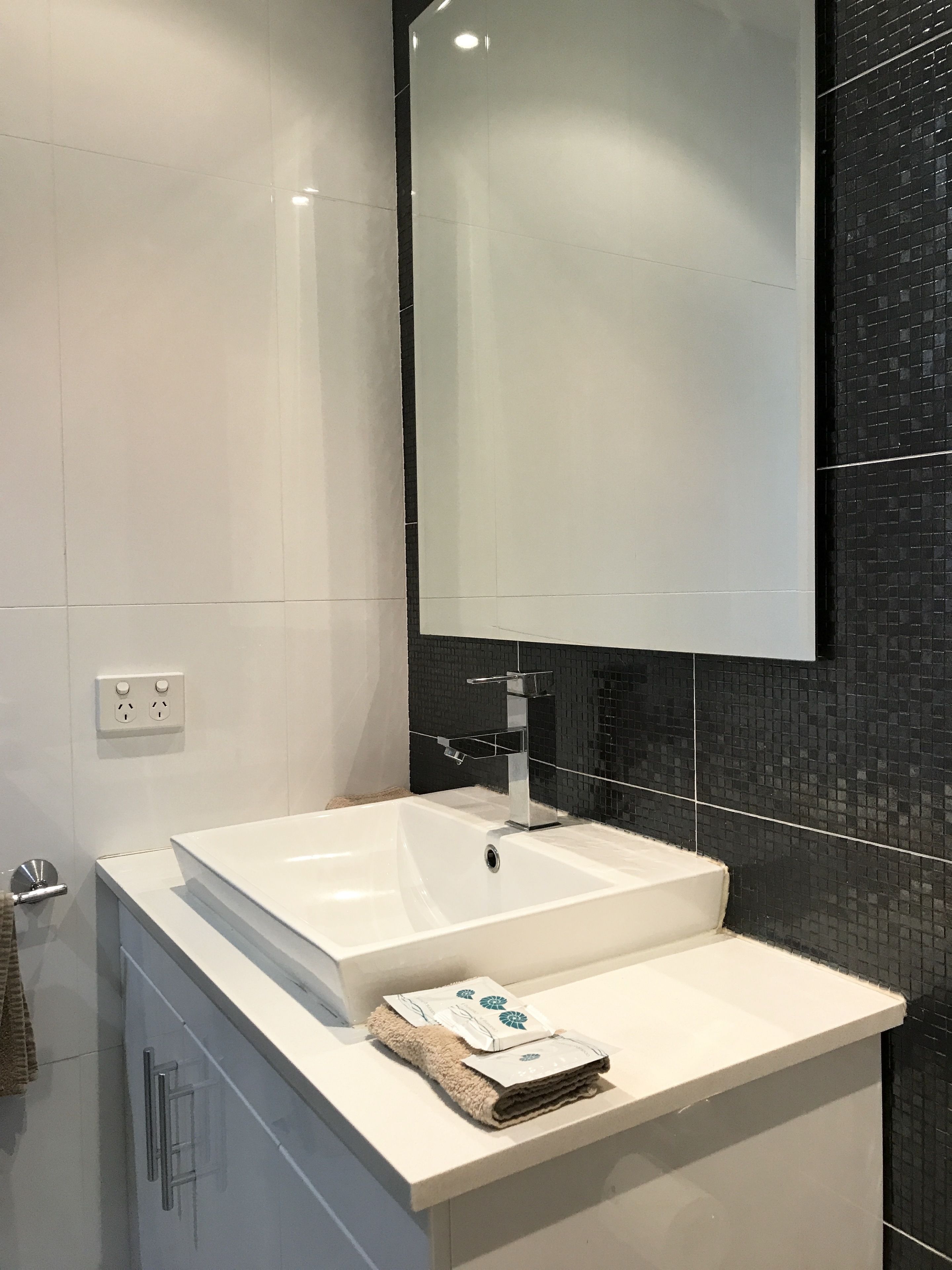 A modern bathroom with a white sink, a mirror, and a black tiled backsplash.