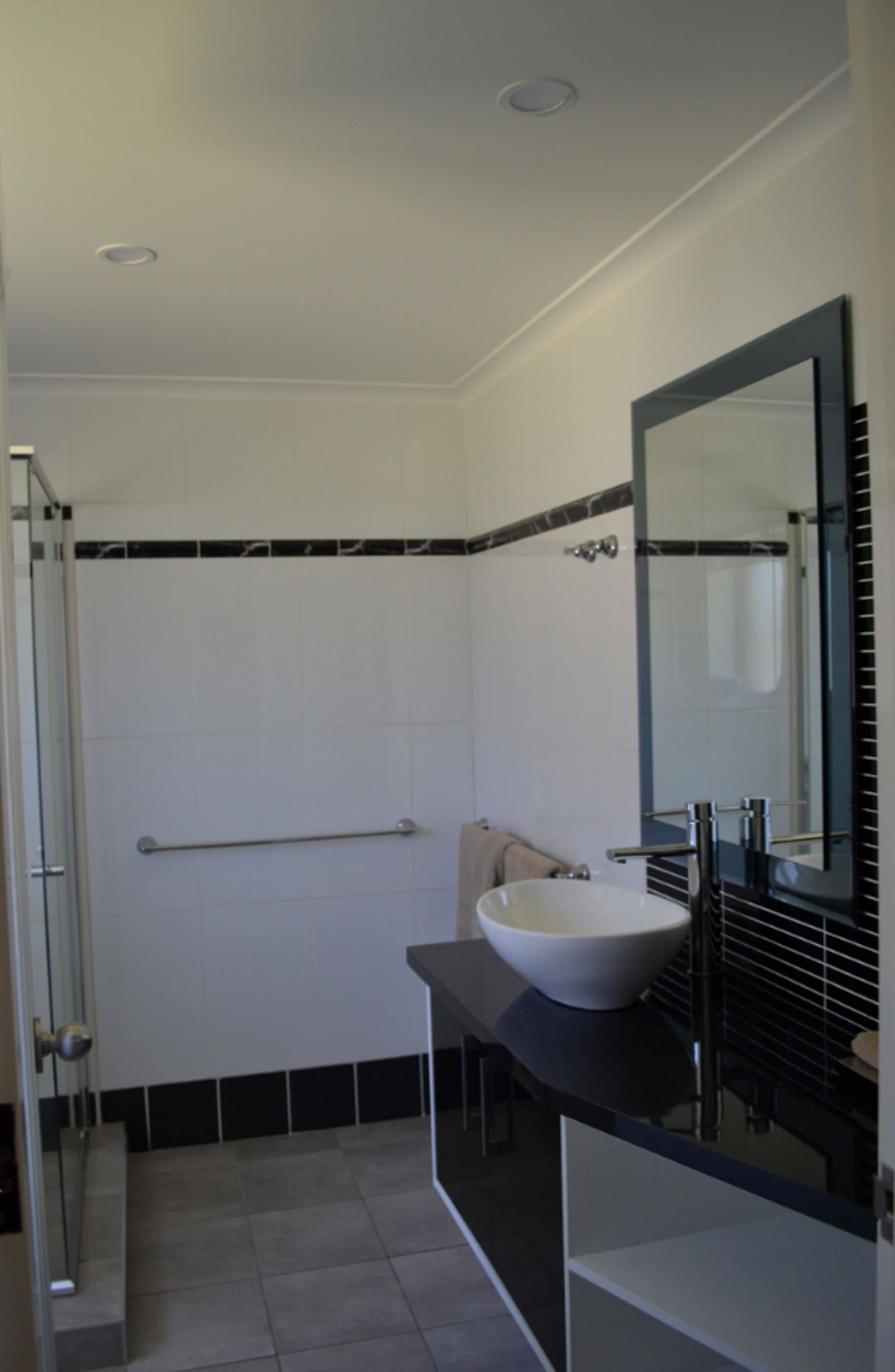 Une salle de bain moderne avec une douche à l’italienne en verre, un lavabo blanc et un grand miroir.