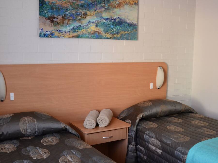Habitación de hotel con dos camas, cabecera de madera, mesita de noche con toallas y un cuadro en la pared.