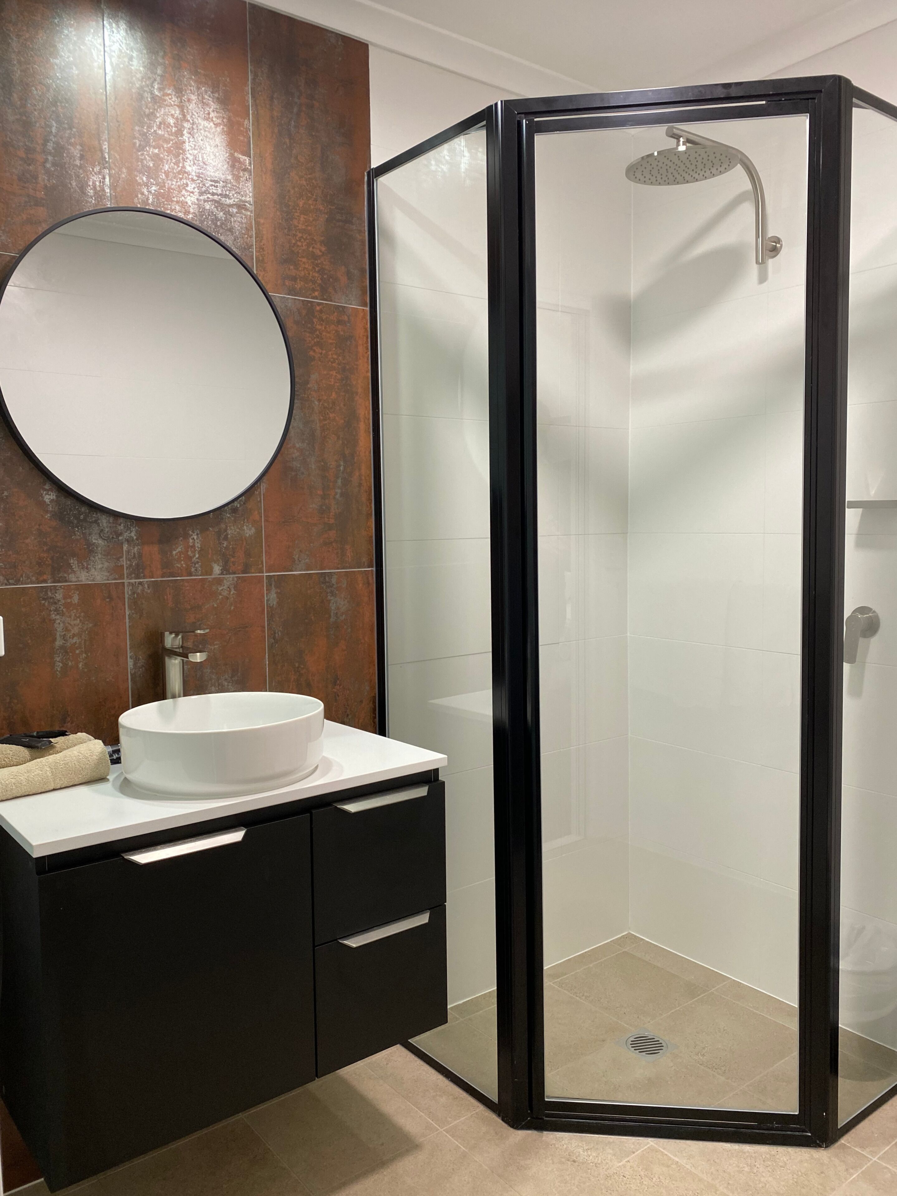 A modern bathroom with a glass-enclosed shower, a round mirror, and a white sink.