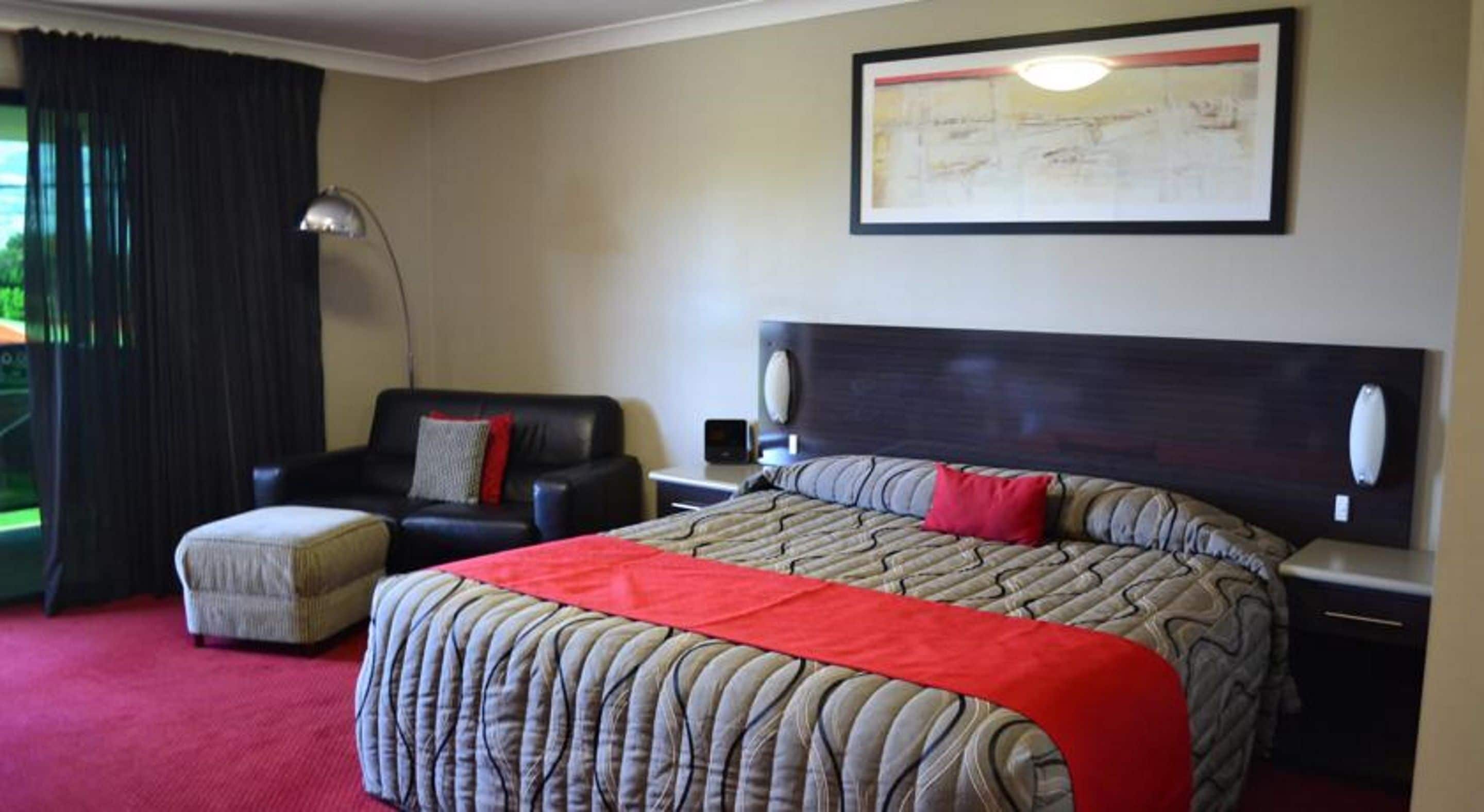 A hotel room with a large bed, a chair, a desk, and a window with curtains.