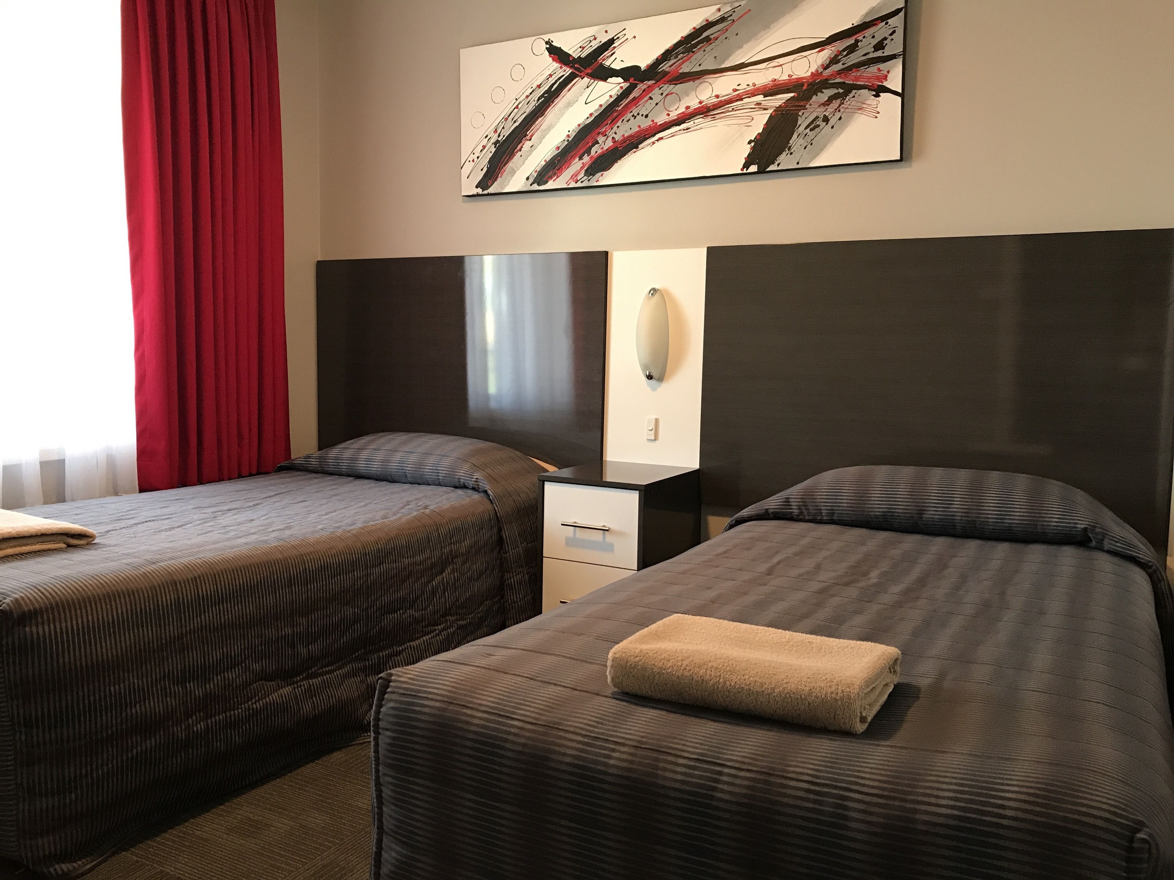 Habitación de hotel con dos camas, una mesita de noche, un espejo y un cuadro en la pared.