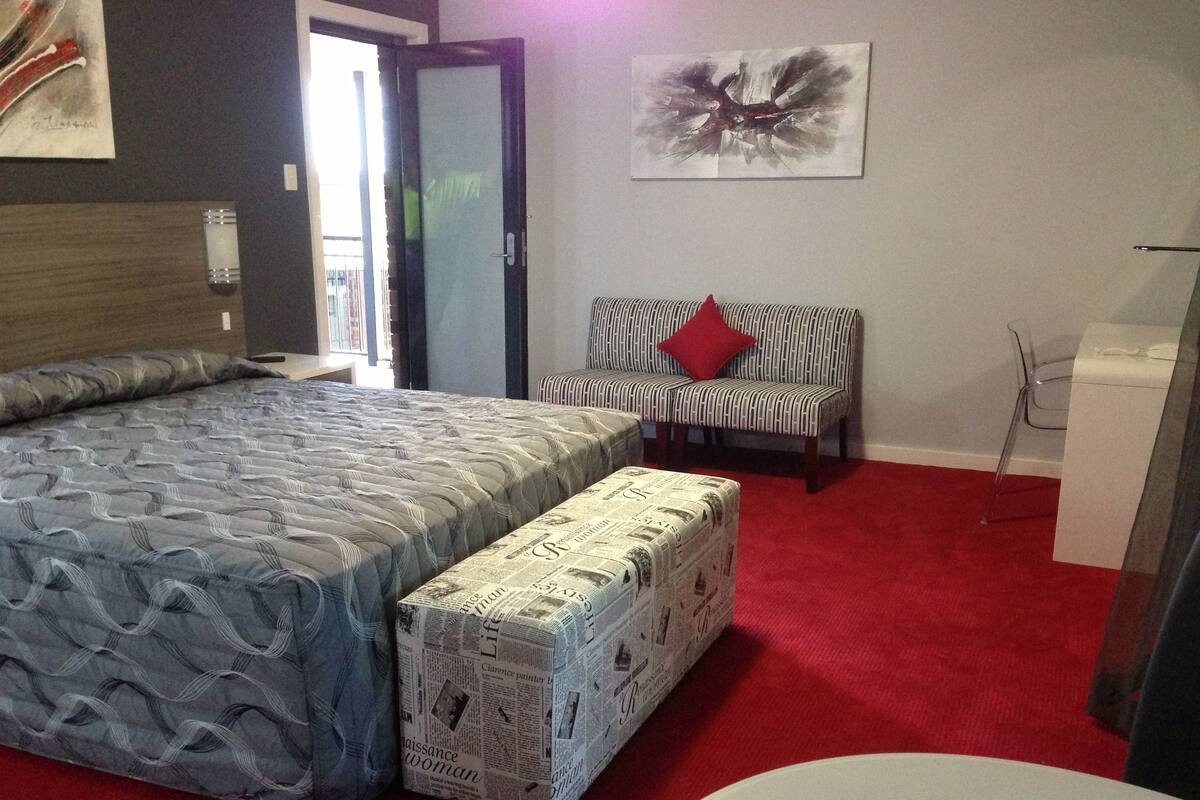 Une chambre avec un grand lit, un canapé, une moquette rouge et un tableau au mur.