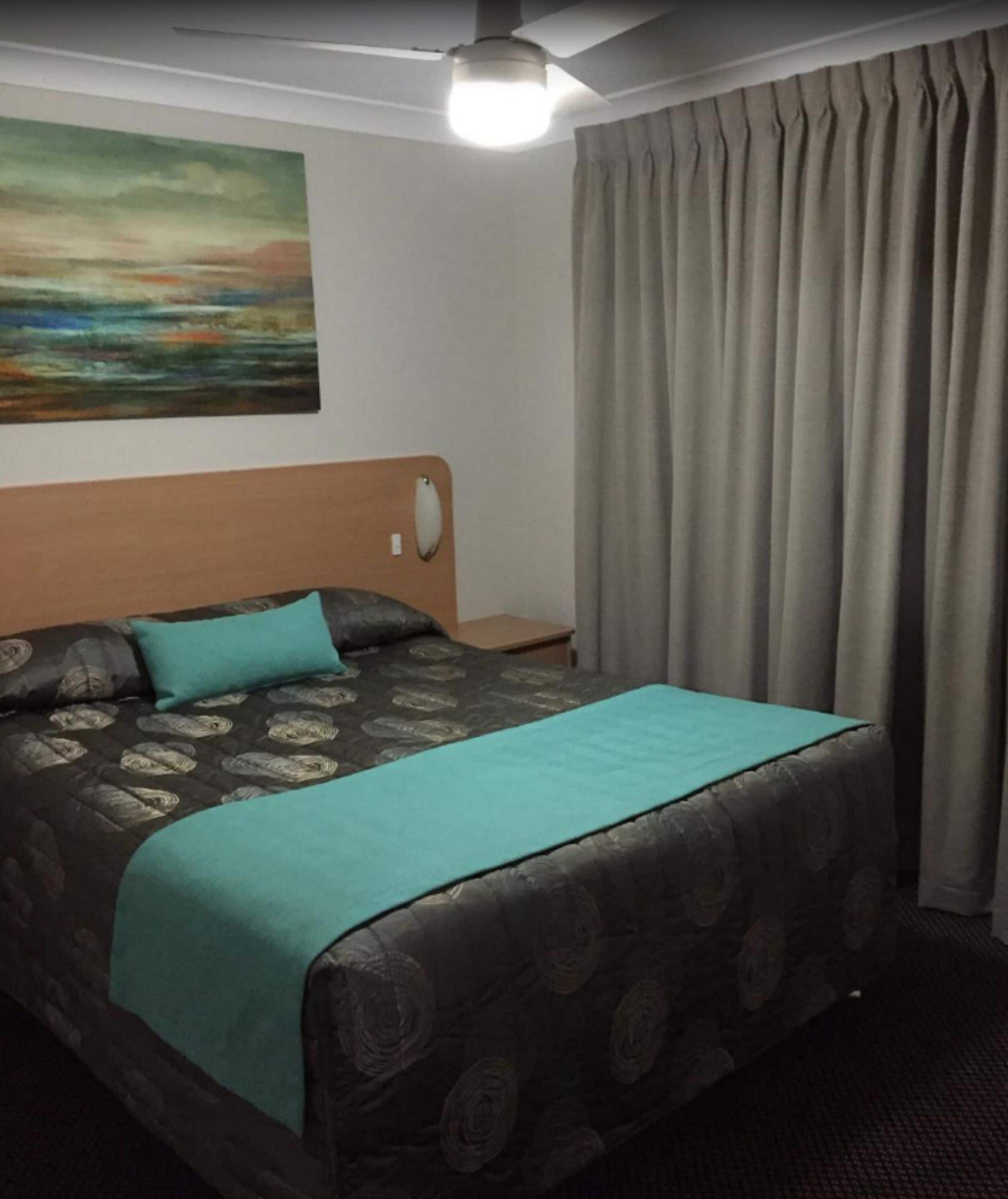 A hotel room with a bed, a headboard, a nightstand, a painting, and a window with curtains.