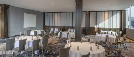 A conference room with multiple round tables, chairs, and a projector screen.