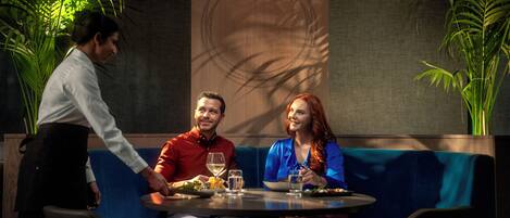 A restaurant with a blue booth seating area, a waiter serving a meal, and a decorative wall with a circular pattern.