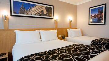 A hotel room with two beds, a large framed picture of a cityscape, and two wall-mounted lamps.