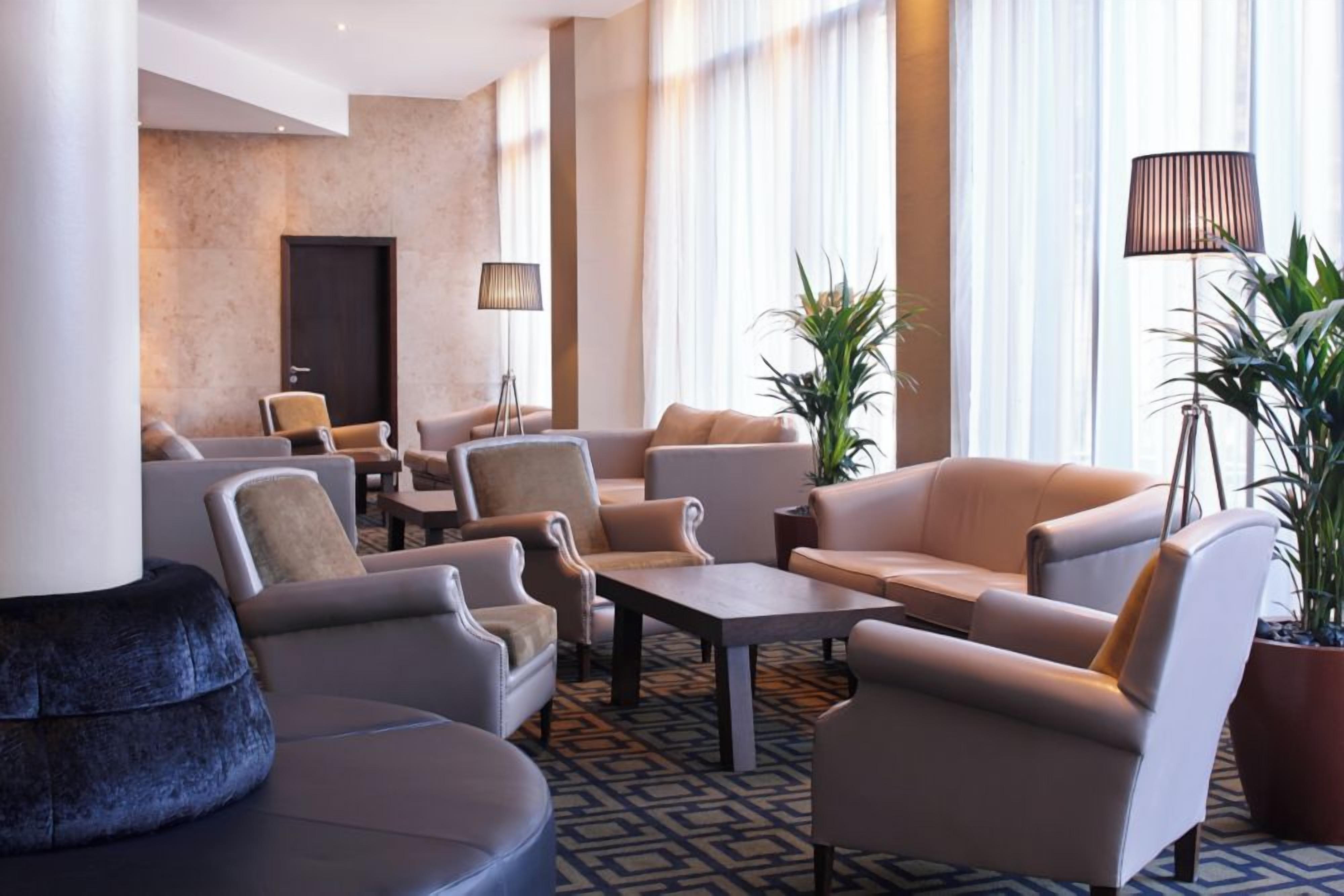 Un vestíbulo de hotel con arreglos de asientos, una mesa de centro y plantas en macetas.