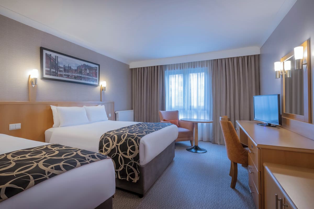 A hotel room with two beds, a desk with a television, a chair, and a window with curtains.