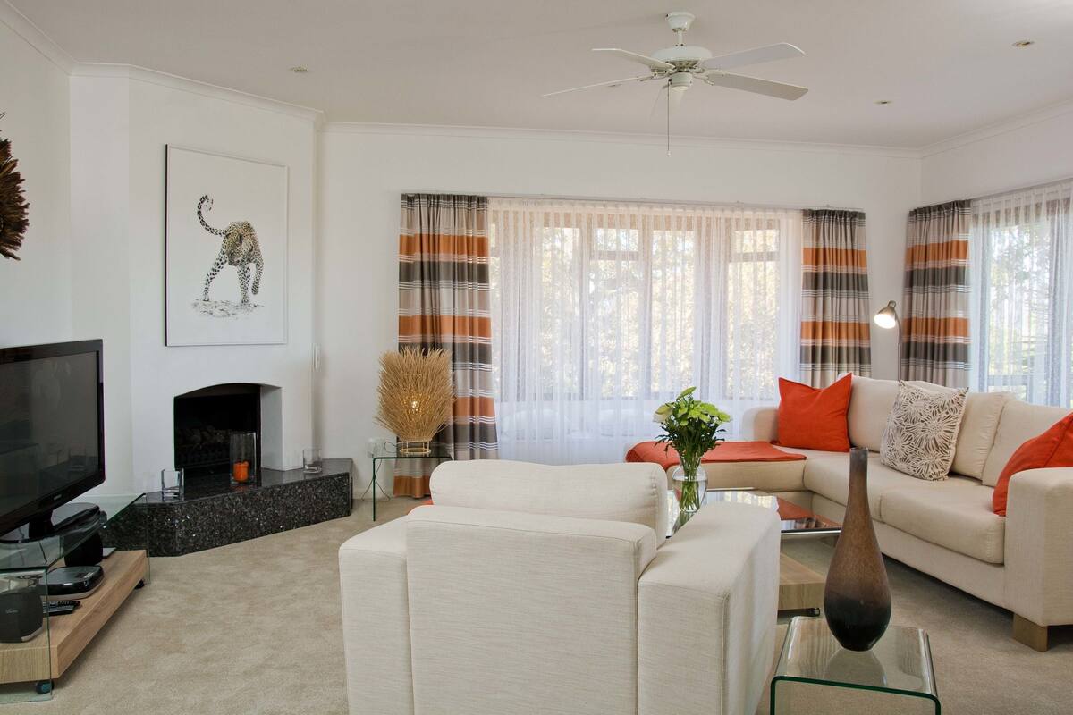 A modern living room with a flat-screen TV, a fireplace, a sofa set, and striped curtains.