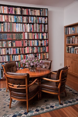 A library with a wooden table and leather chairs surrounded by bookshelves filled with books.