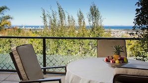 A balcony with a table and chairs, a bowl of fruit, and a view of a city and ocean. - At Winkfield House (Cape Town)