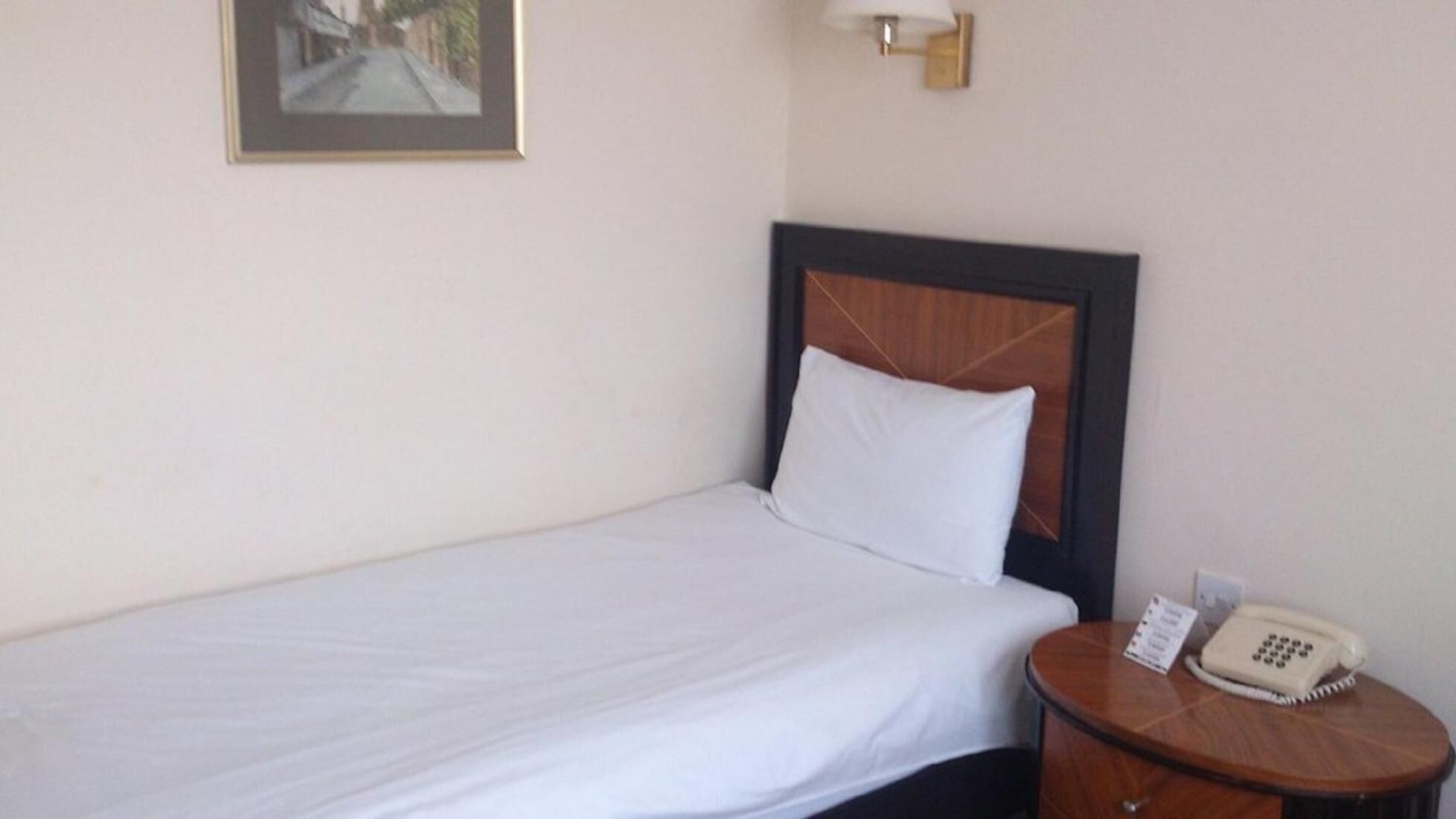 A single bed with a wooden headboard, a bedside table with a telephone, and a framed picture on the wall.