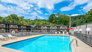 A swimming pool with lounge chairs and a fenced area, surrounded by a motel building with a red umbrella and a sign.