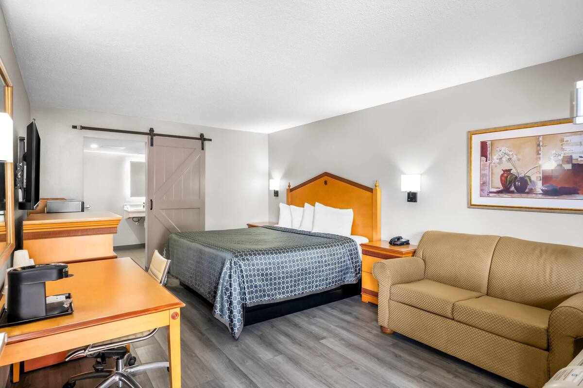 A hotel room with a bed, a desk, a sofa, and a painting on the wall.