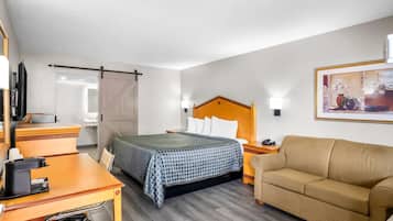 A hotel room with a bed, a desk, a sofa, and a painting on the wall.