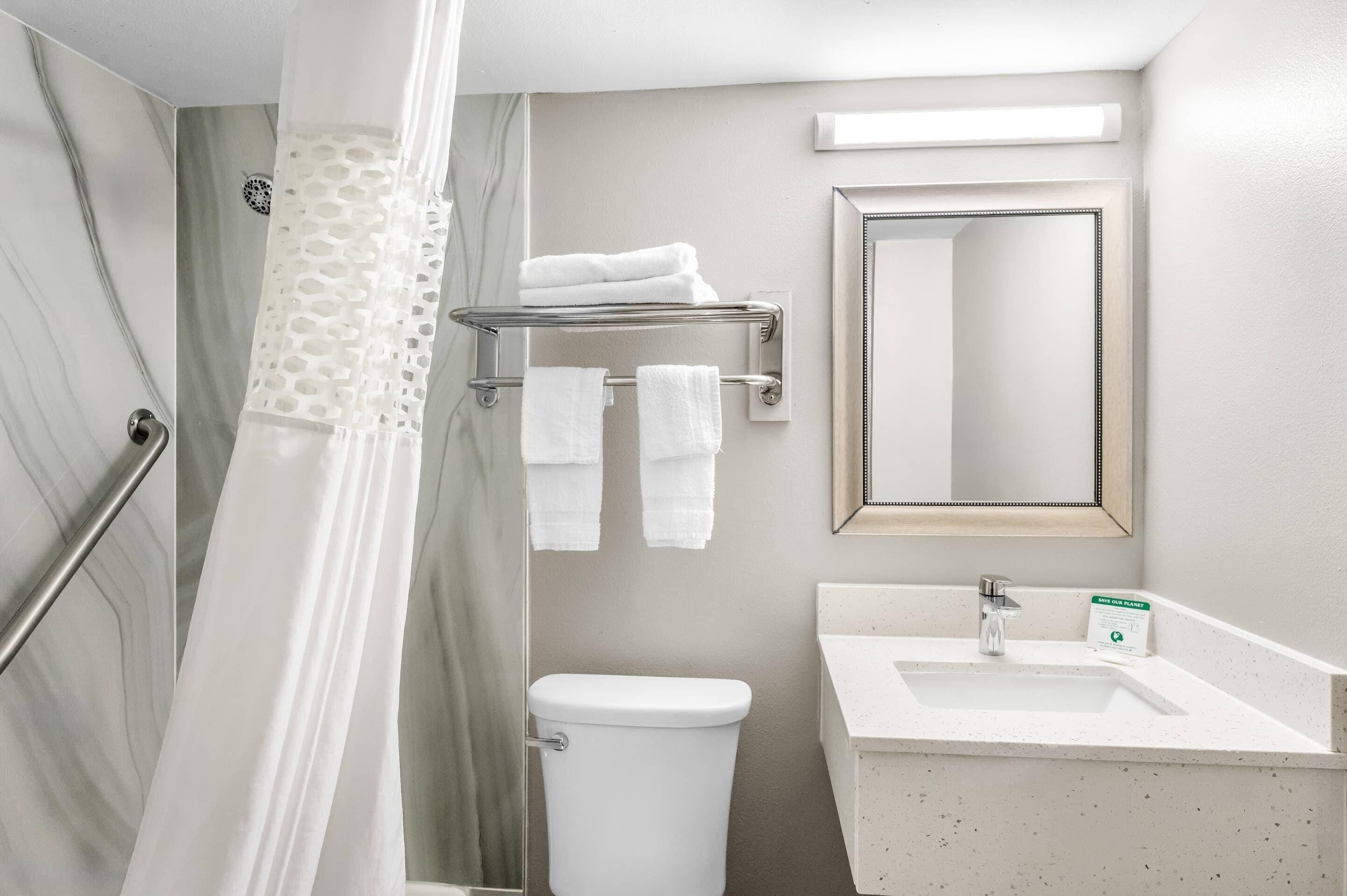 A bathroom with a shower, toilet, sink, and a towel rack.