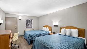 A hotel room with two beds, a desk, a chair, and a door.