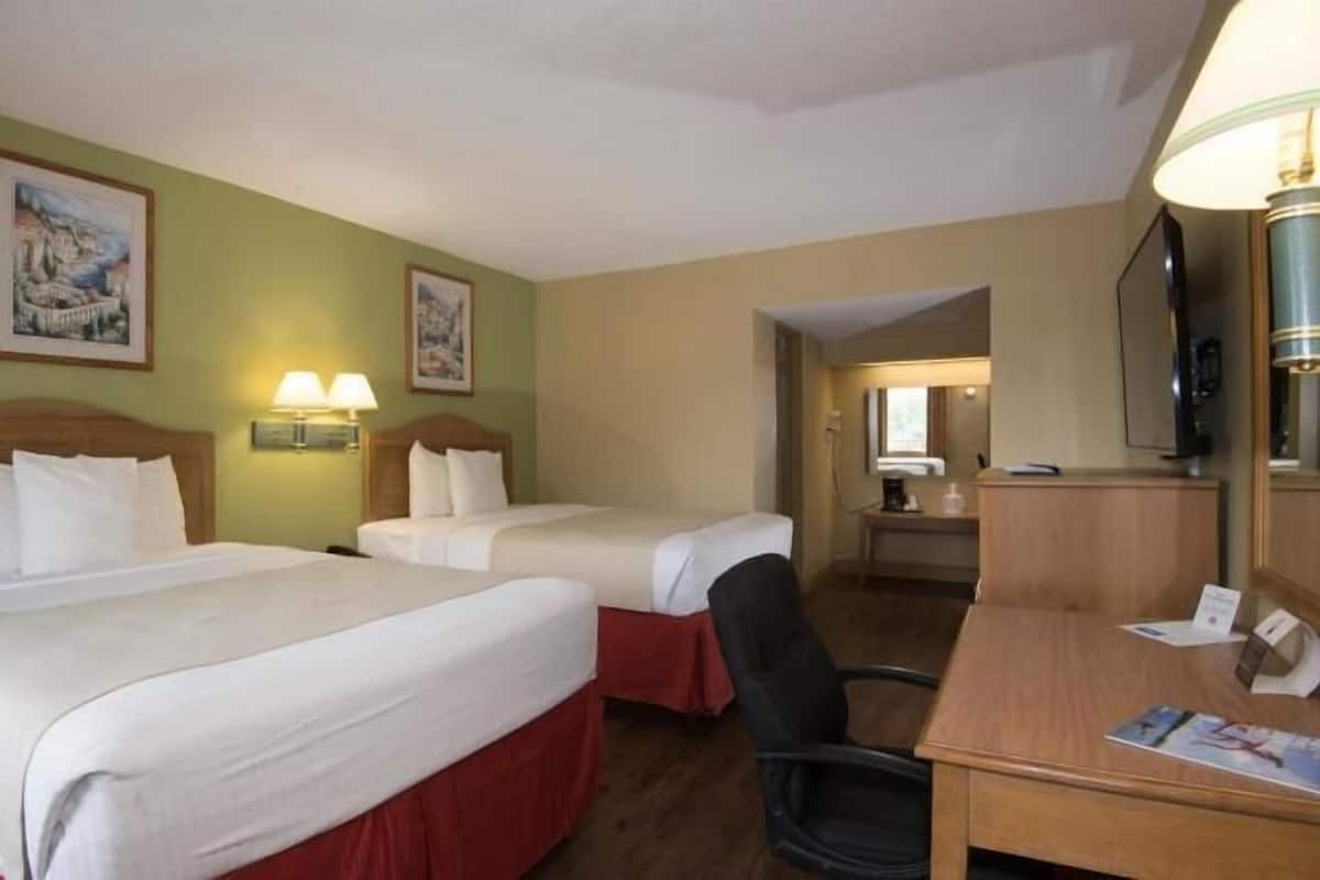 A hotel room with two beds, a desk, a chair, a lamp, and a television.