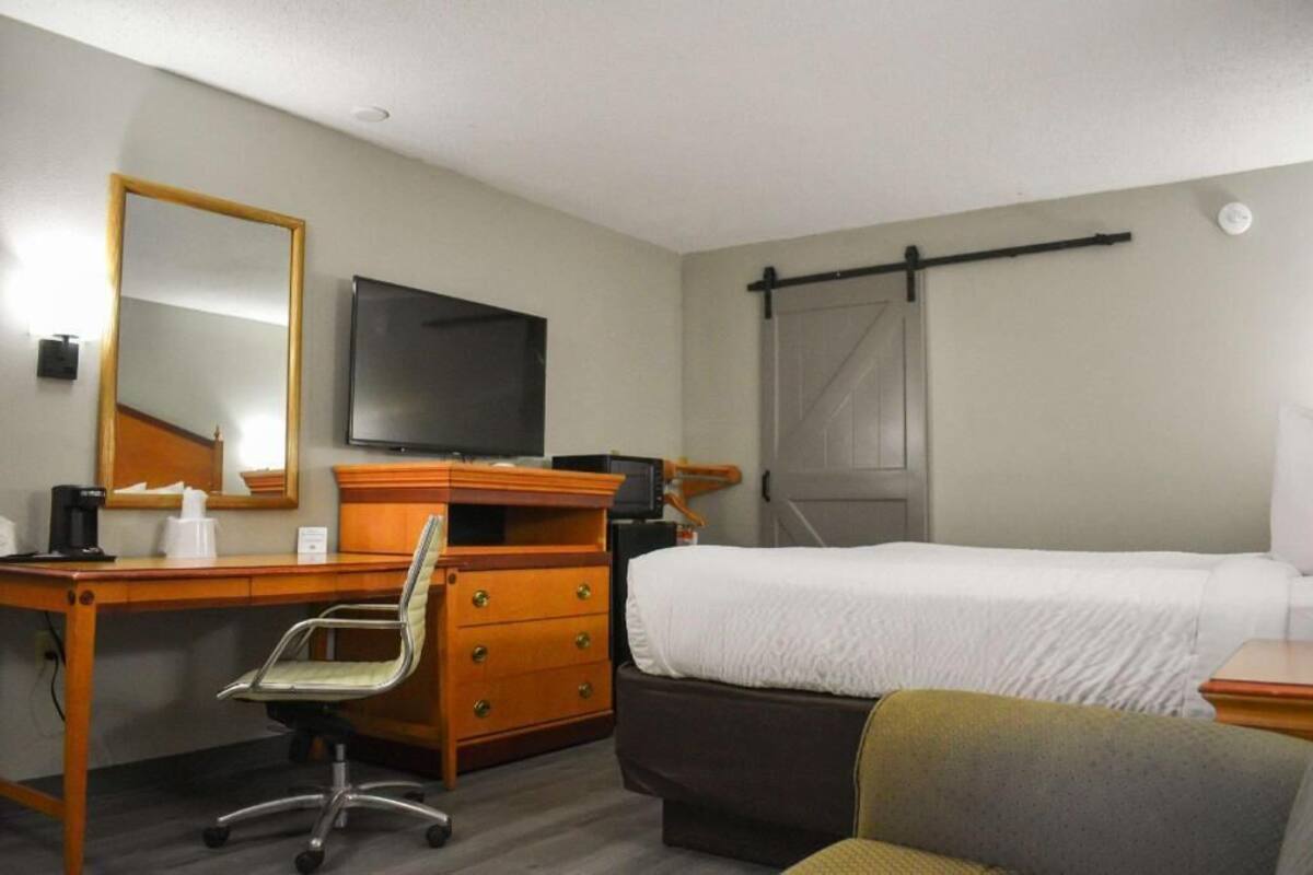 A hotel room with a bed, a desk with a chair, a television, a wardrobe, and a window with a curtain.