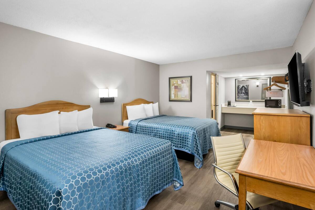 A hotel room with two beds, a desk, a chair, a TV, and a mirror.