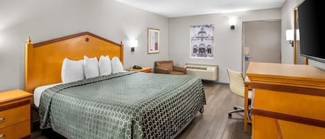 A hotel room with a wooden bed, a desk, a chair, a television, and a poster on the wall.