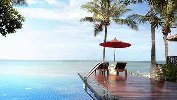A poolside area with a red umbrella, lounge chairs, and palm trees.