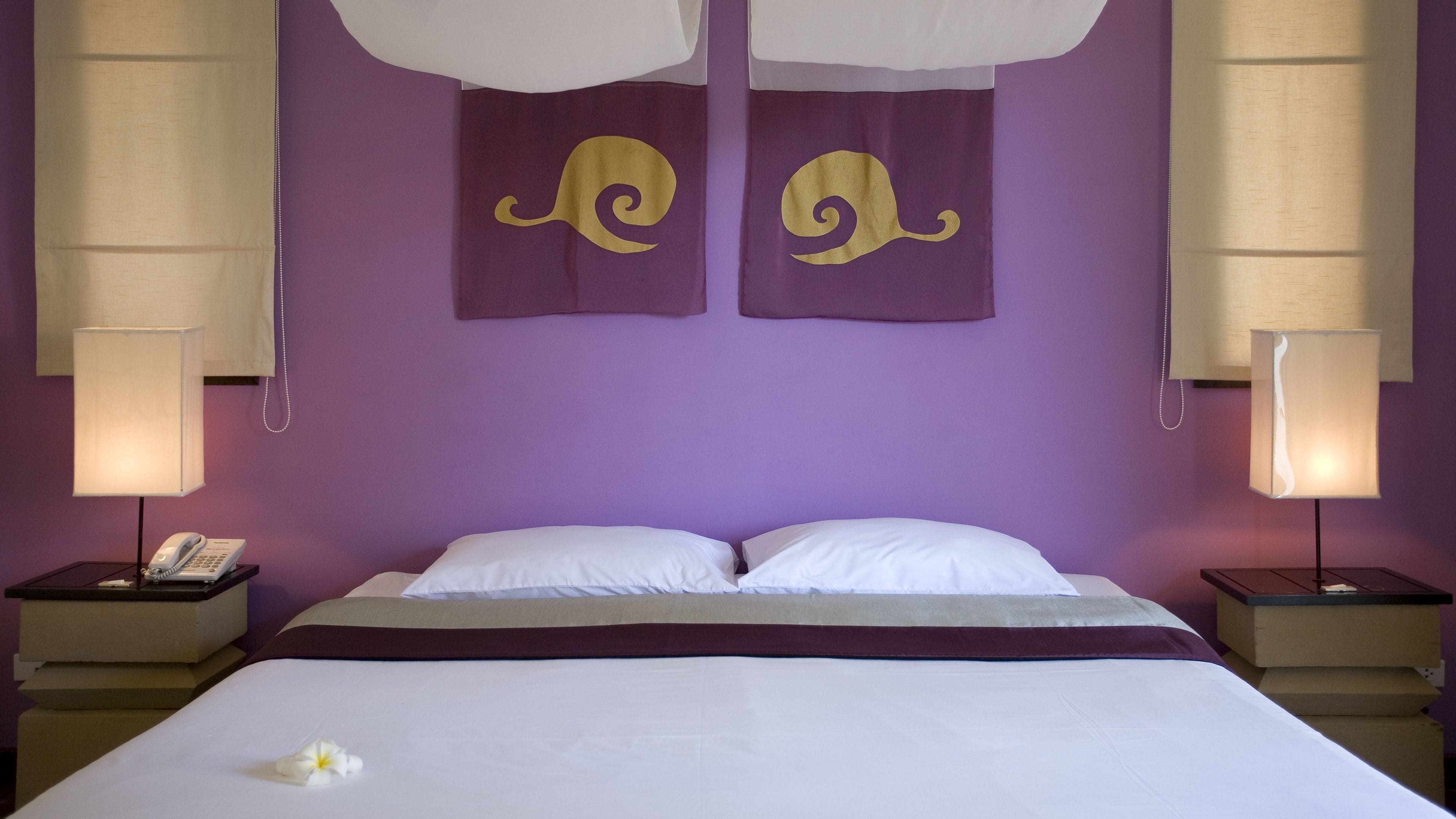A hotel room with a large bed, two nightstands, a telephone, and two wall-mounted lamps.