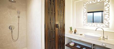 Un baño con ducha, un lavabo con un espejo decorativo y un tocador con estante.