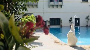 A pool area with a water feature, surrounded by lush greenery and a building with traditional architecture.