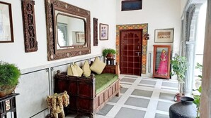 A room with a large mirror, a sofa with cushions, a wooden cabinet, and a door with a decorative frame. - HOTEL MAHENDRA PRAKASH (Udaipur)