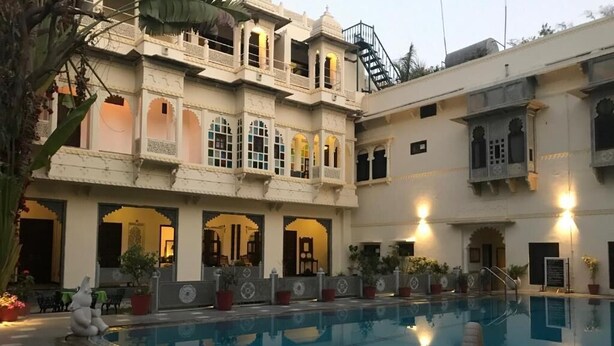 A pool area with a large pool, surrounded by buildings with traditional architecture, including arched windows and balconies. - HOTEL MAHENDRA PRAKASH (Udaipur)