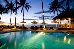 A poolside area with lounge chairs and umbrellas, palm trees, and a view of the ocean at sunset. - Kanok Buri Resort  (Koh Samui)