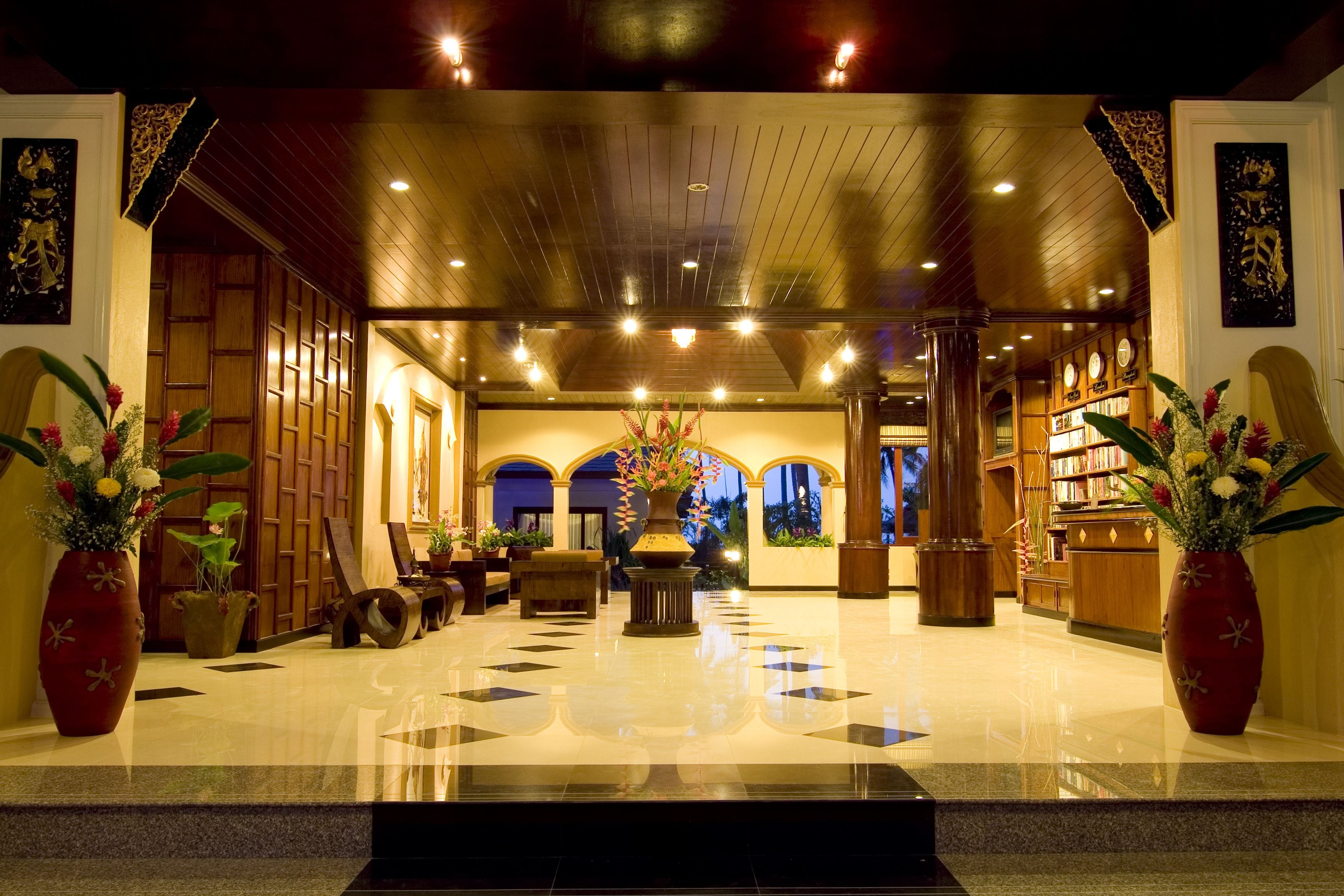 A lobby with a polished floor, wooden furniture, and large vases with flowers.