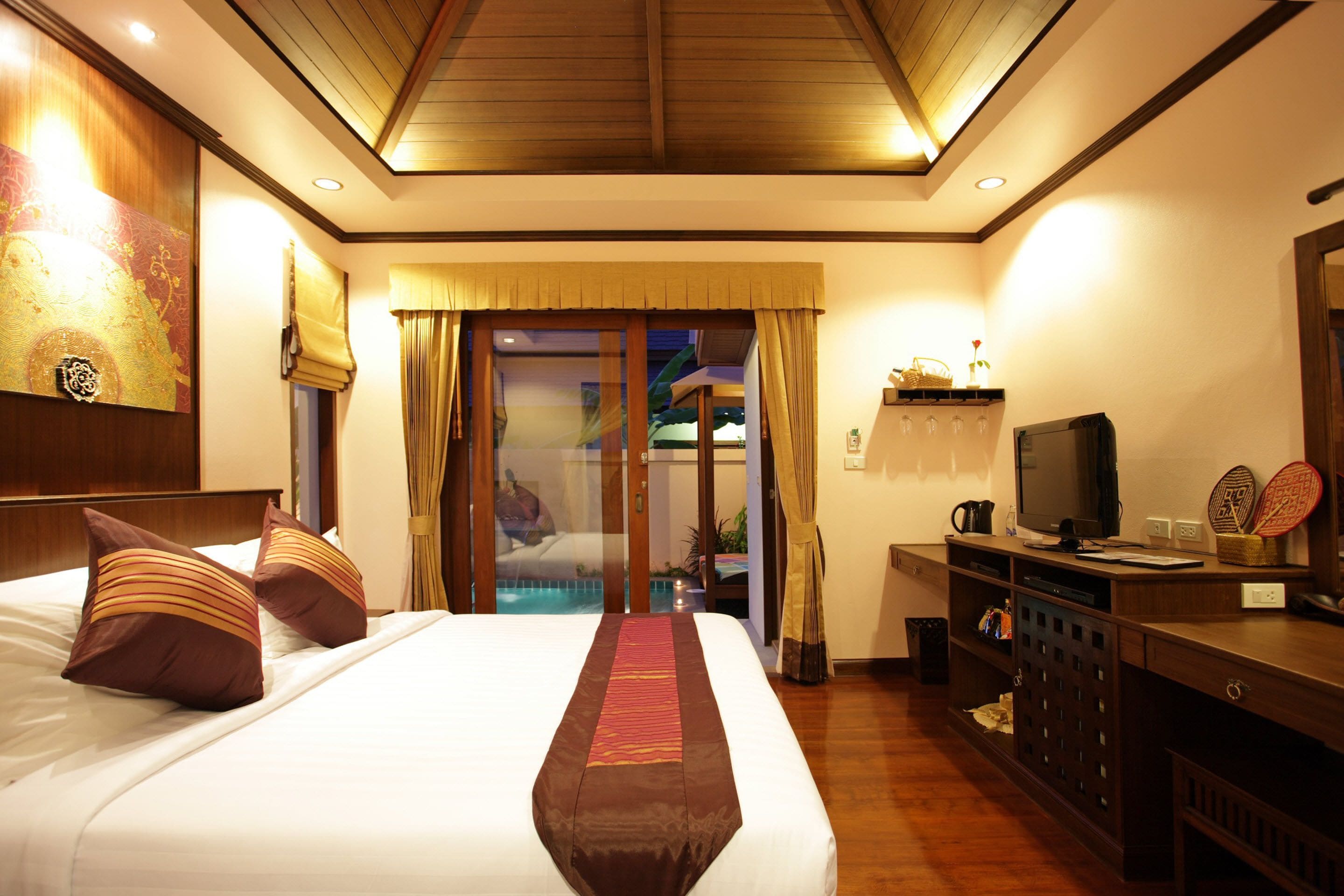 A hotel room with a large bed, a television, a desk with a computer, and a view of a pool through the glass door.
