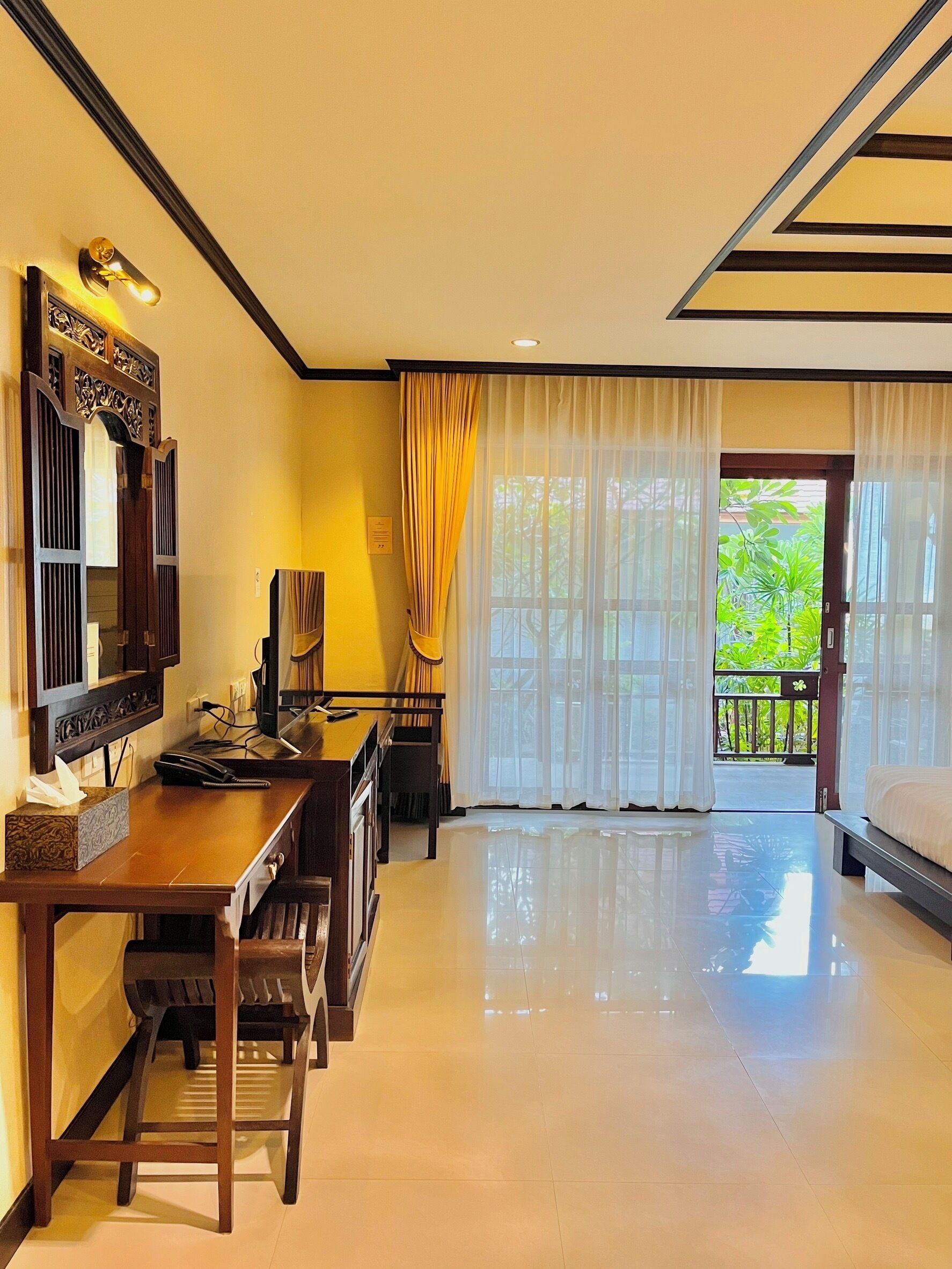 Une chambre d’hôtel avec un bureau en bois, une télévision et un balcon doté de rideaux.