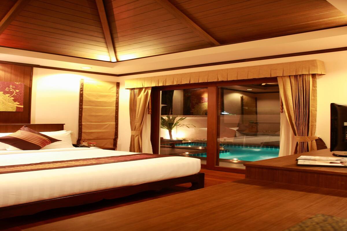 A hotel room with a large bed, a wooden floor, a TV, a desk, and a view of a pool.