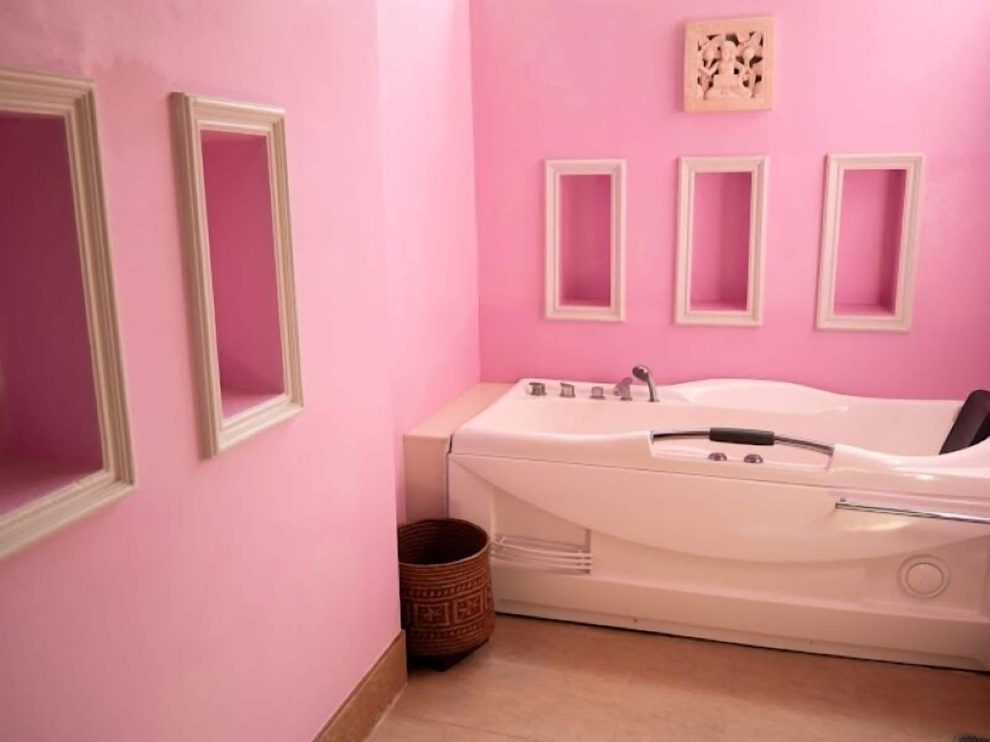 A bathroom with a white bathtub, pink walls, and three framed pictures on the wall.