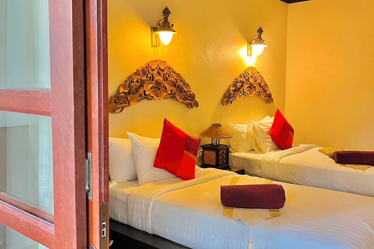 A hotel room with two beds, a wooden door, and wall-mounted lamps.
