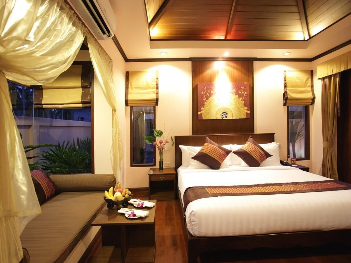 A hotel room with a bed, bedside tables, a sofa, and a window with curtains.