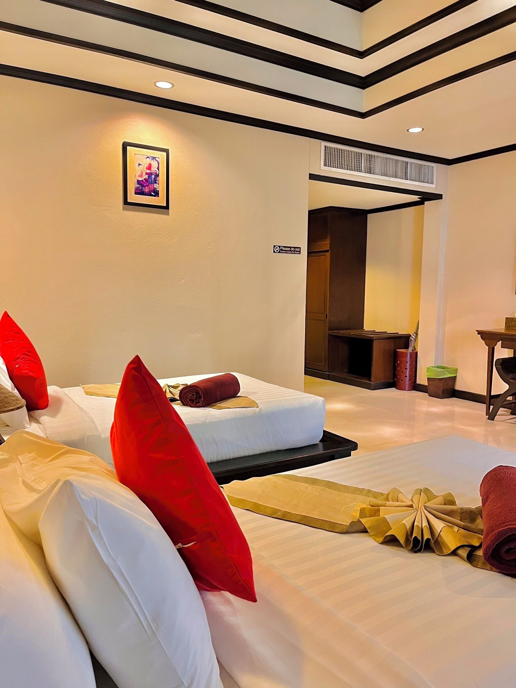 A hotel room with two beds, each with red and white pillows, a framed picture on the wall, and a 'Please do not' sign.