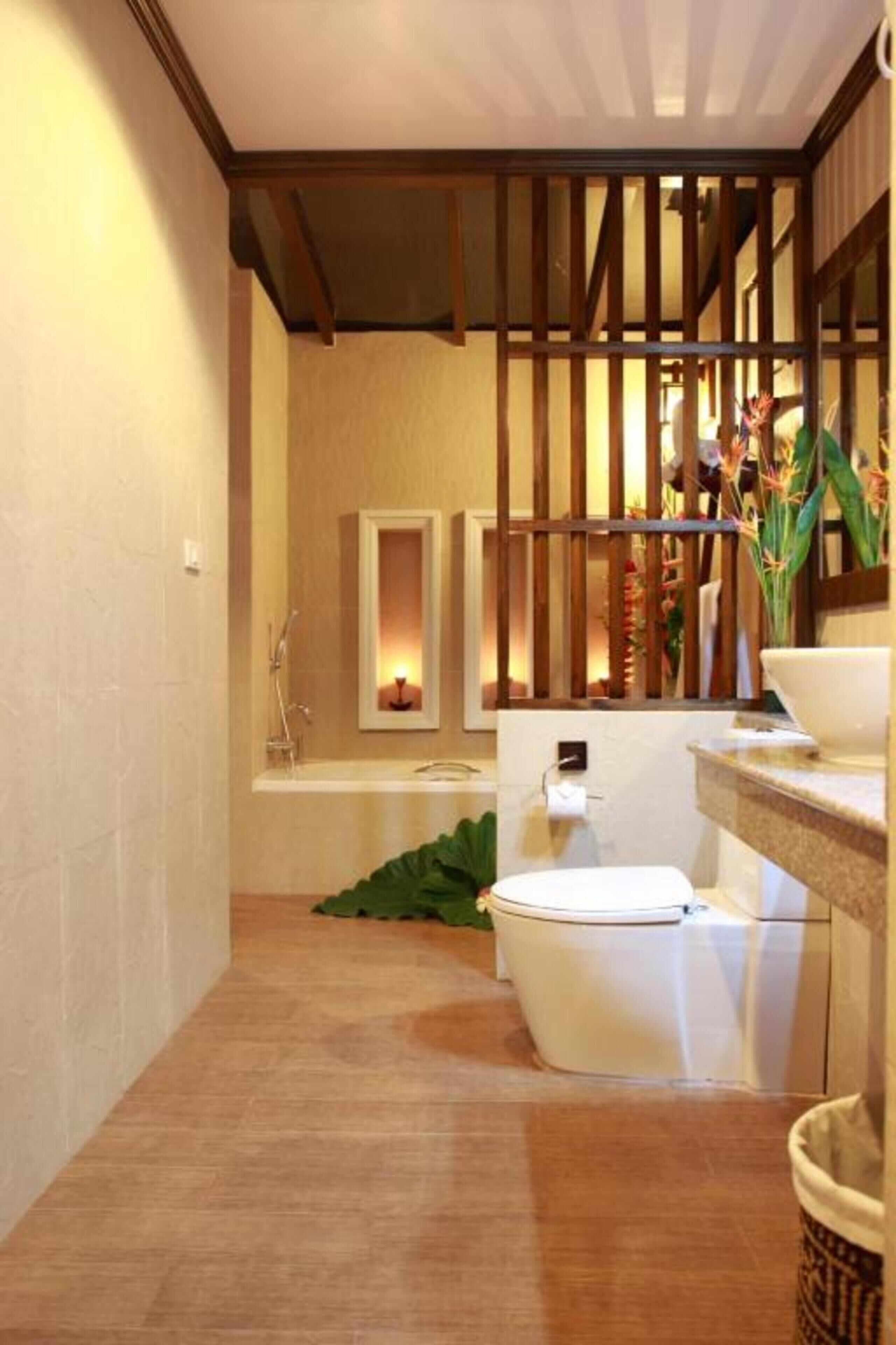 A modern bathroom with a wooden ceiling, a white toilet, a sink with a mirror, and a small plant.