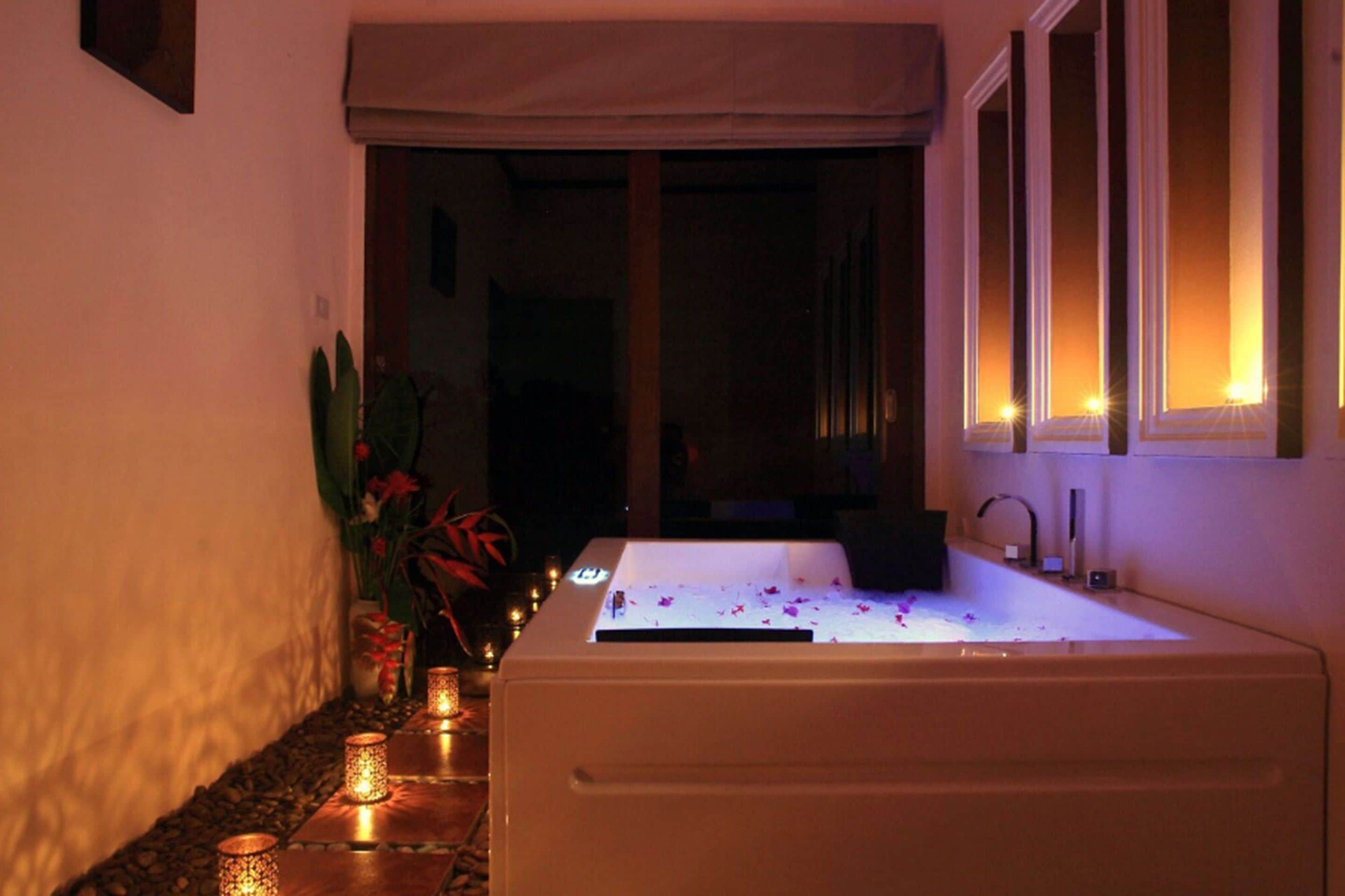 A spa area with a bathtub, candles, and a window with curtains.