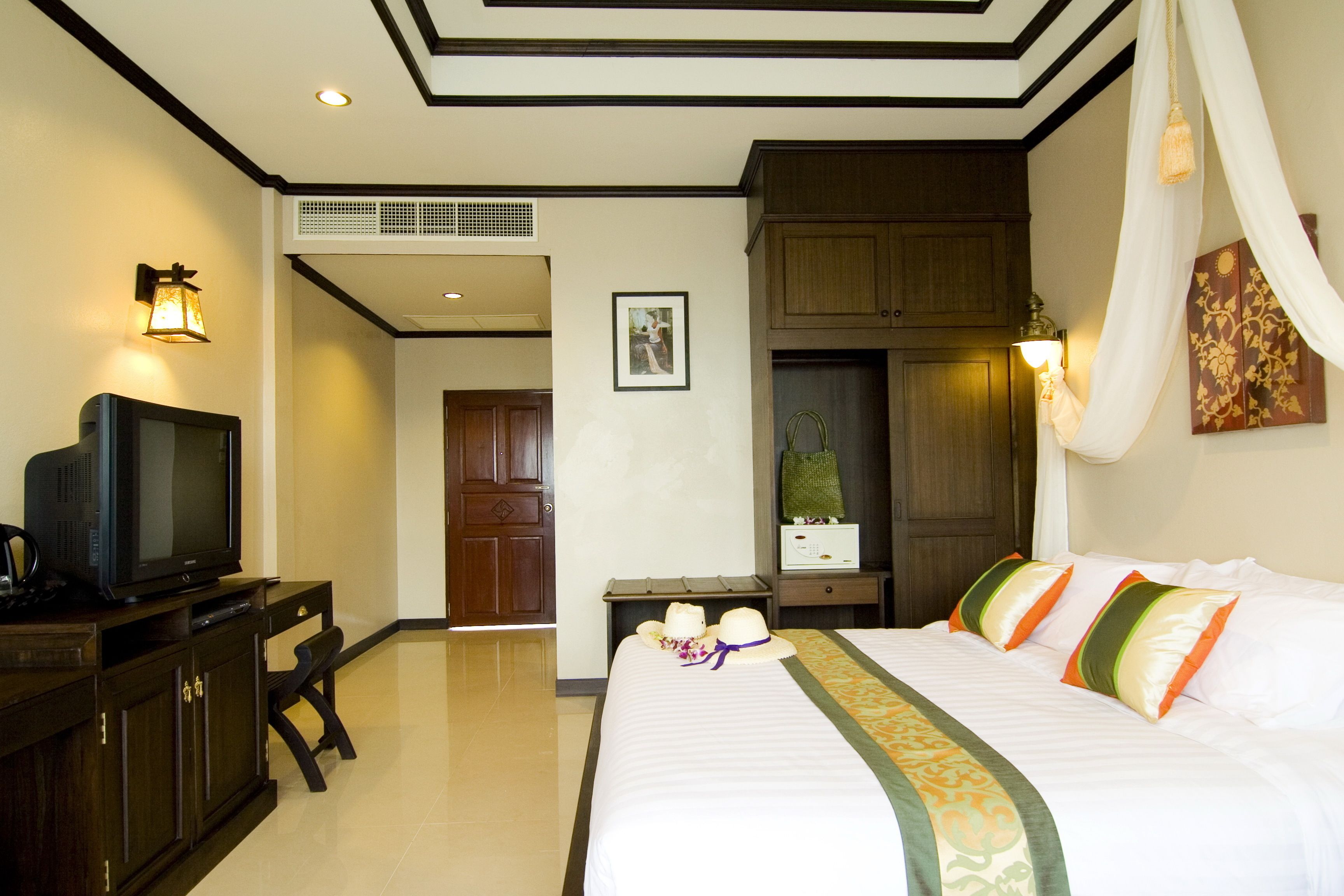 Habitación de hotel con una cama, un televisor sobre un escritorio, un armario y una puerta que da a otra habitación.