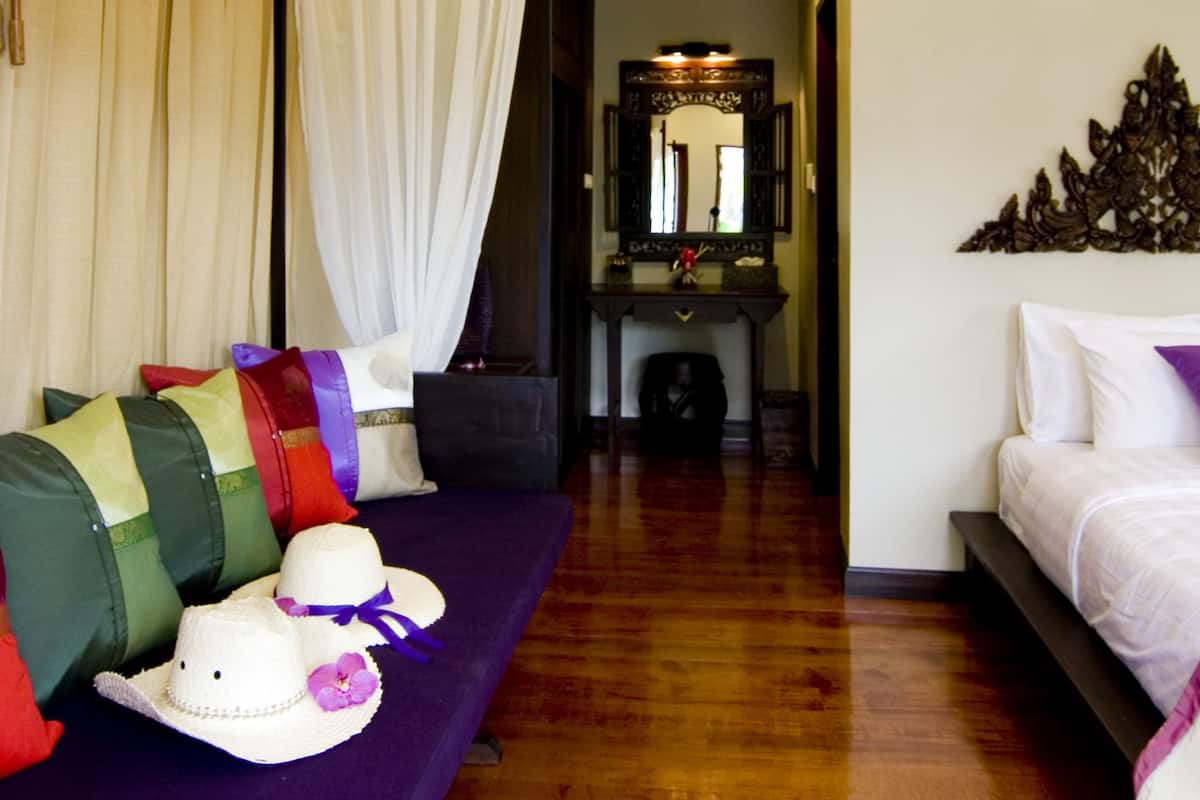 A hotel room with a purple sofa, a bed, a mirror, and a wooden floor.