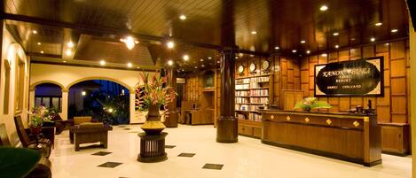 A lobby with a reception desk, bookshelves, seating area, and a large clock.