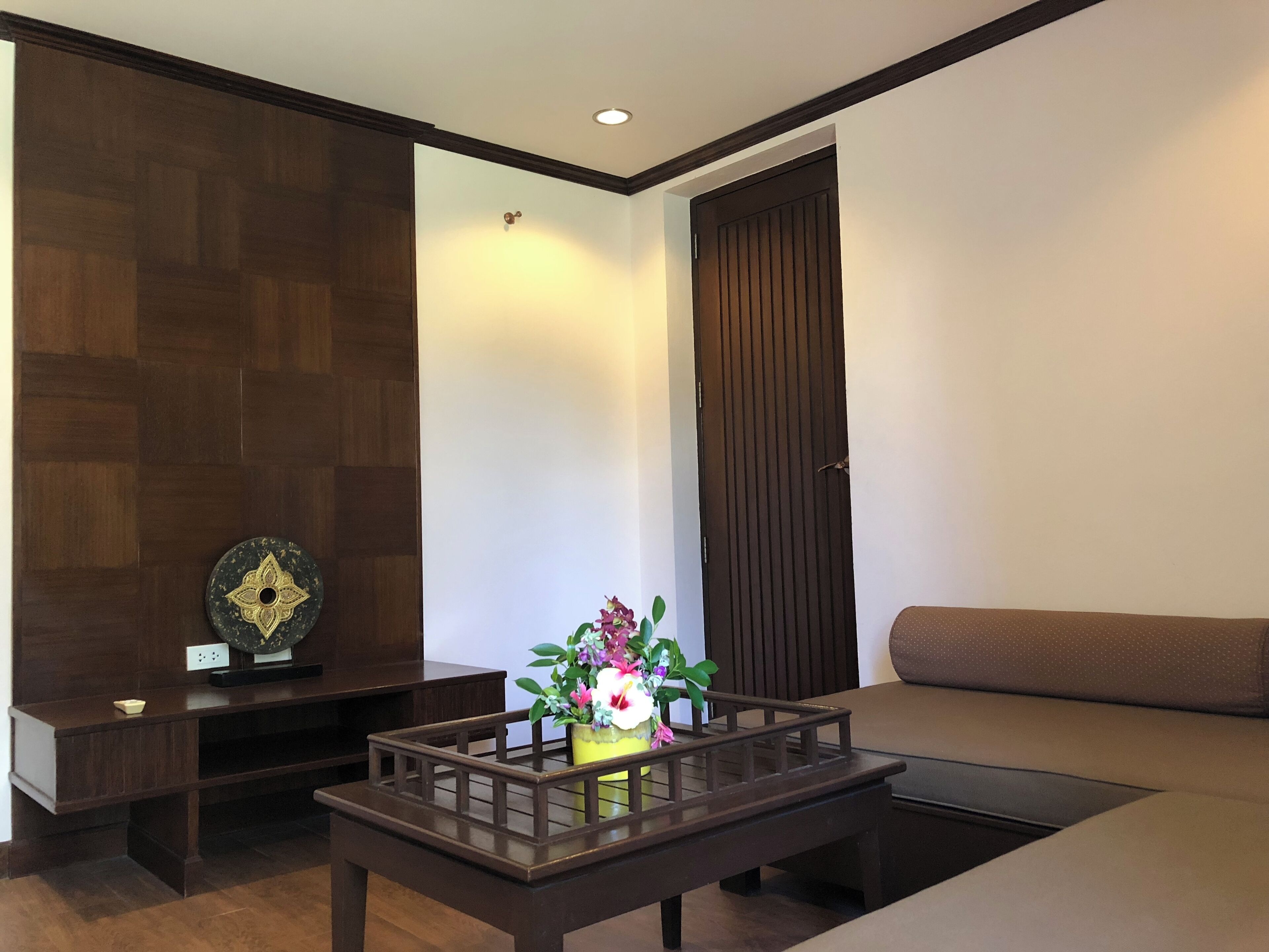 Una sala de estar moderna con piso de madera oscura, un sofá marrón, una mesa de centro con un florero y un mueble de madera oscura.