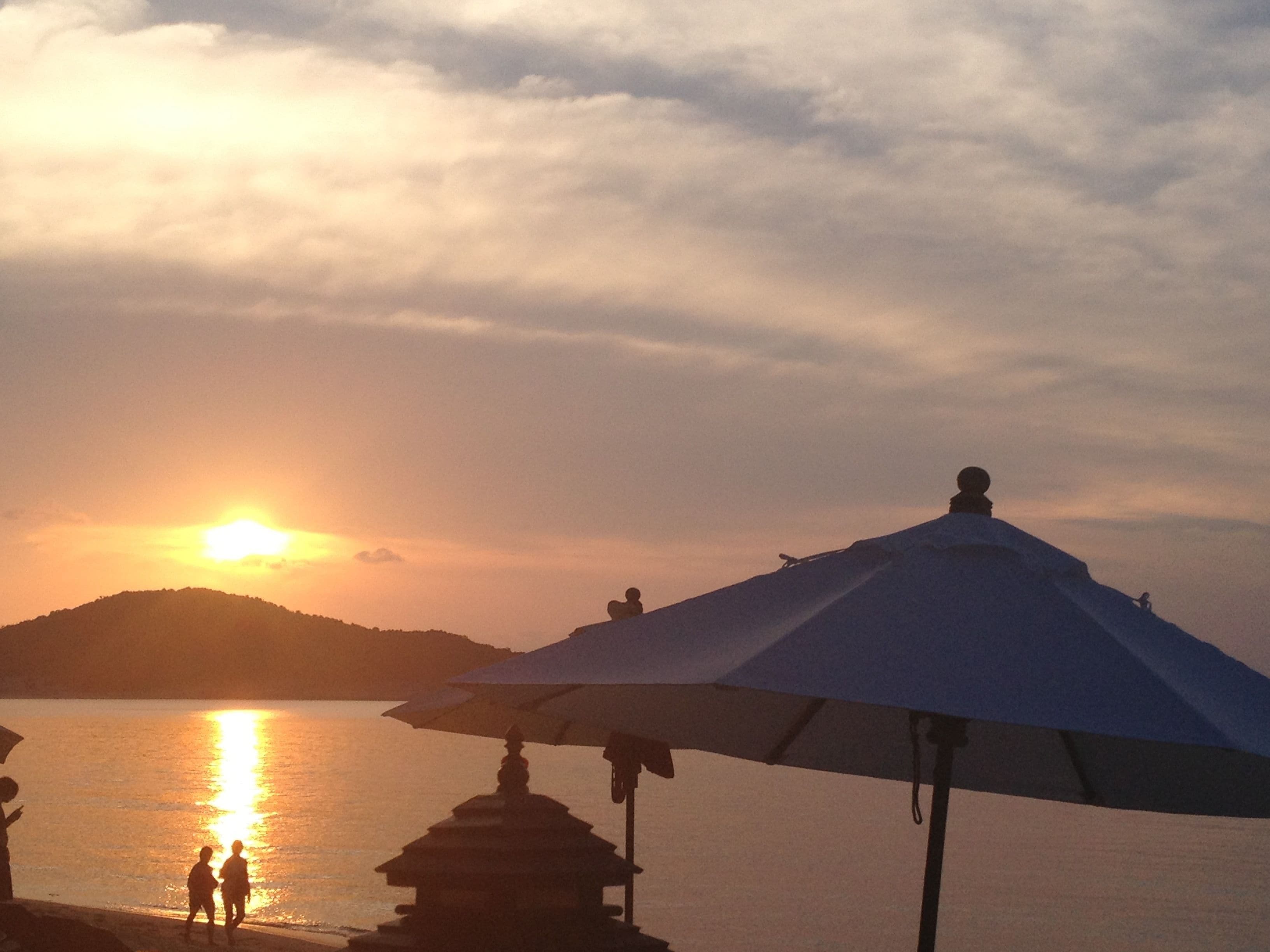 En strandscene med solnedgang, en stor parasol og en tempelbygning.